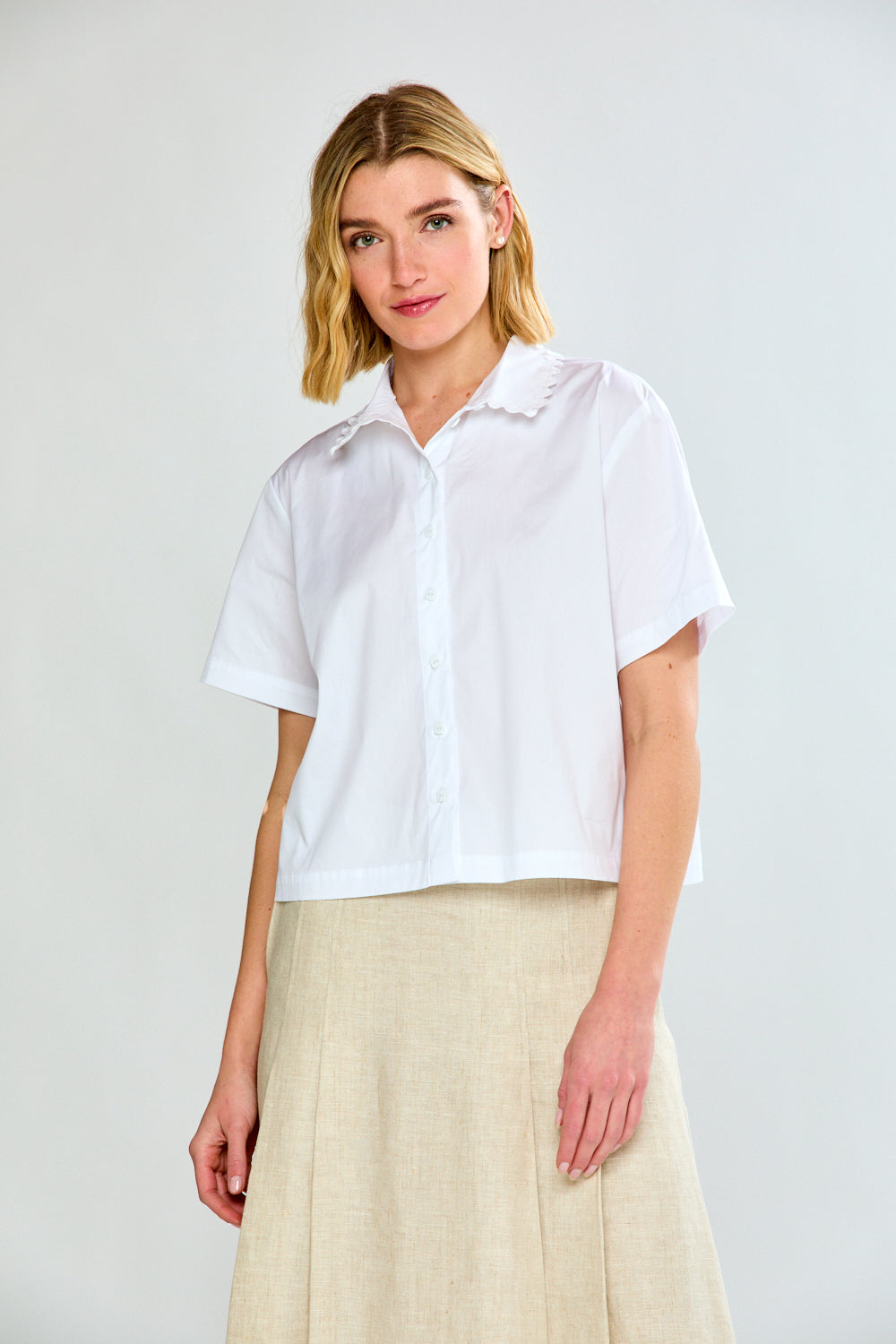 Woman wearing a white short-sleeve shirt and beige skirt on a light gray background