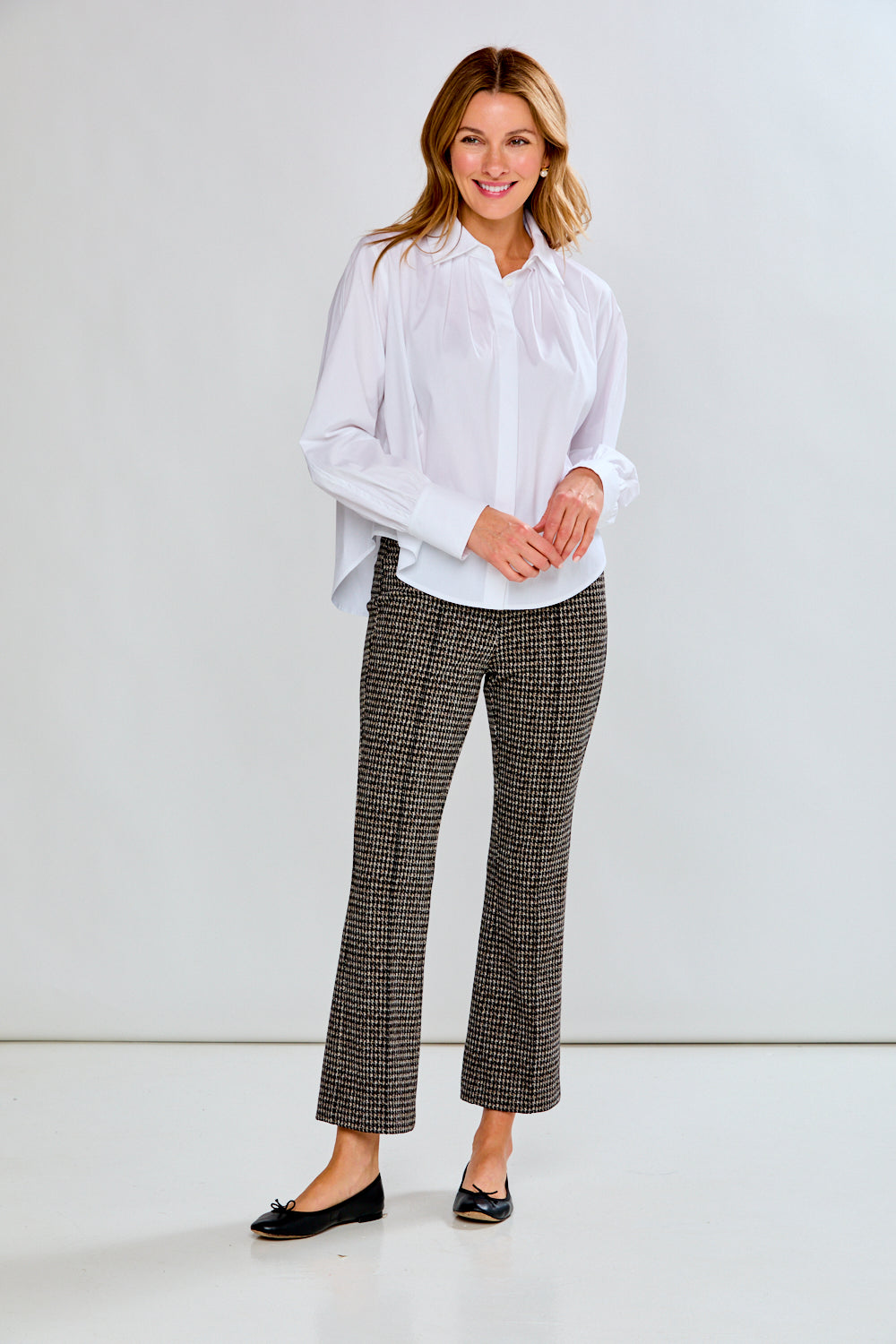 Woman wearing a white blouse and patterned pants against a plain background