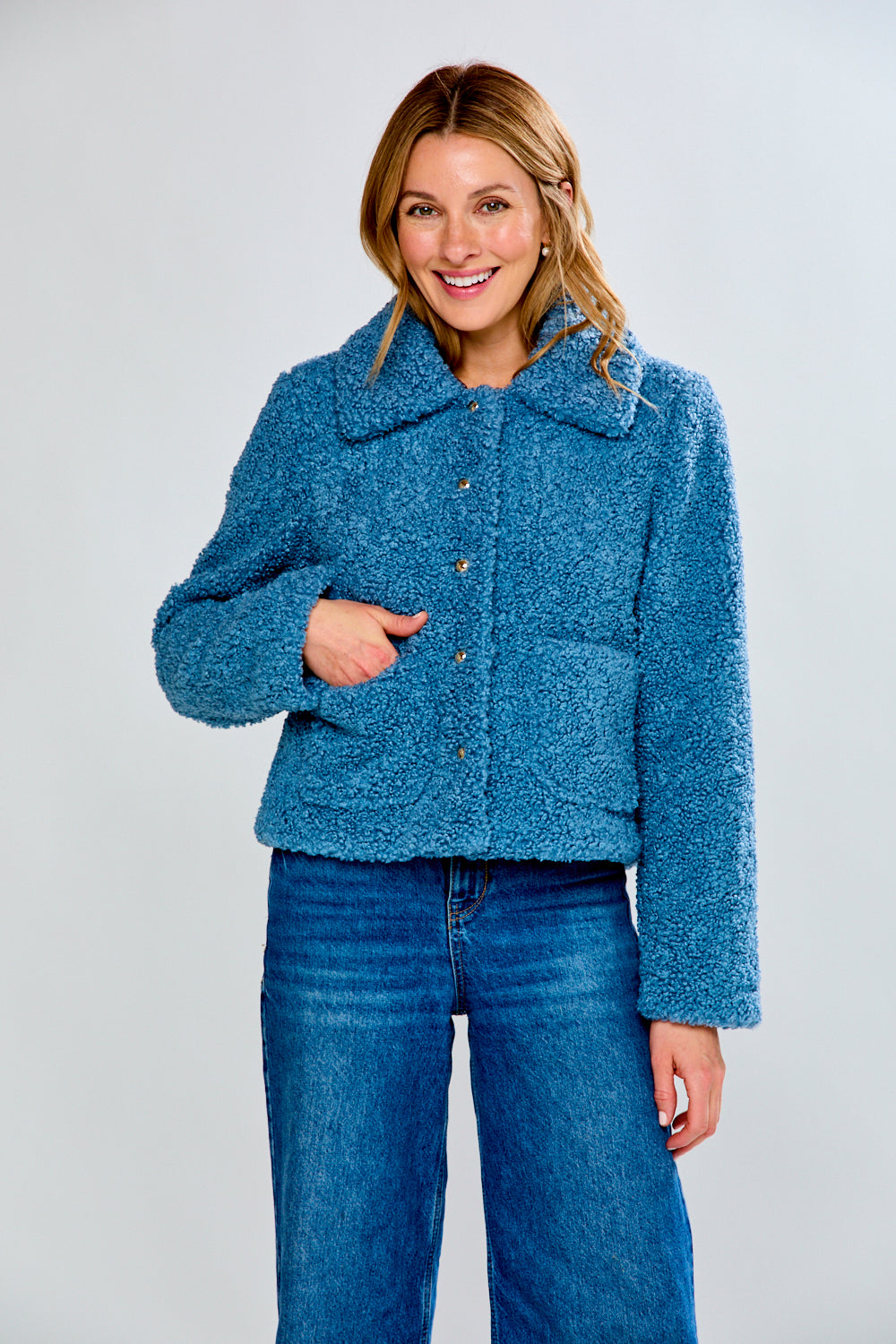 Woman wearing a blue textured jacket and jeans on a white background