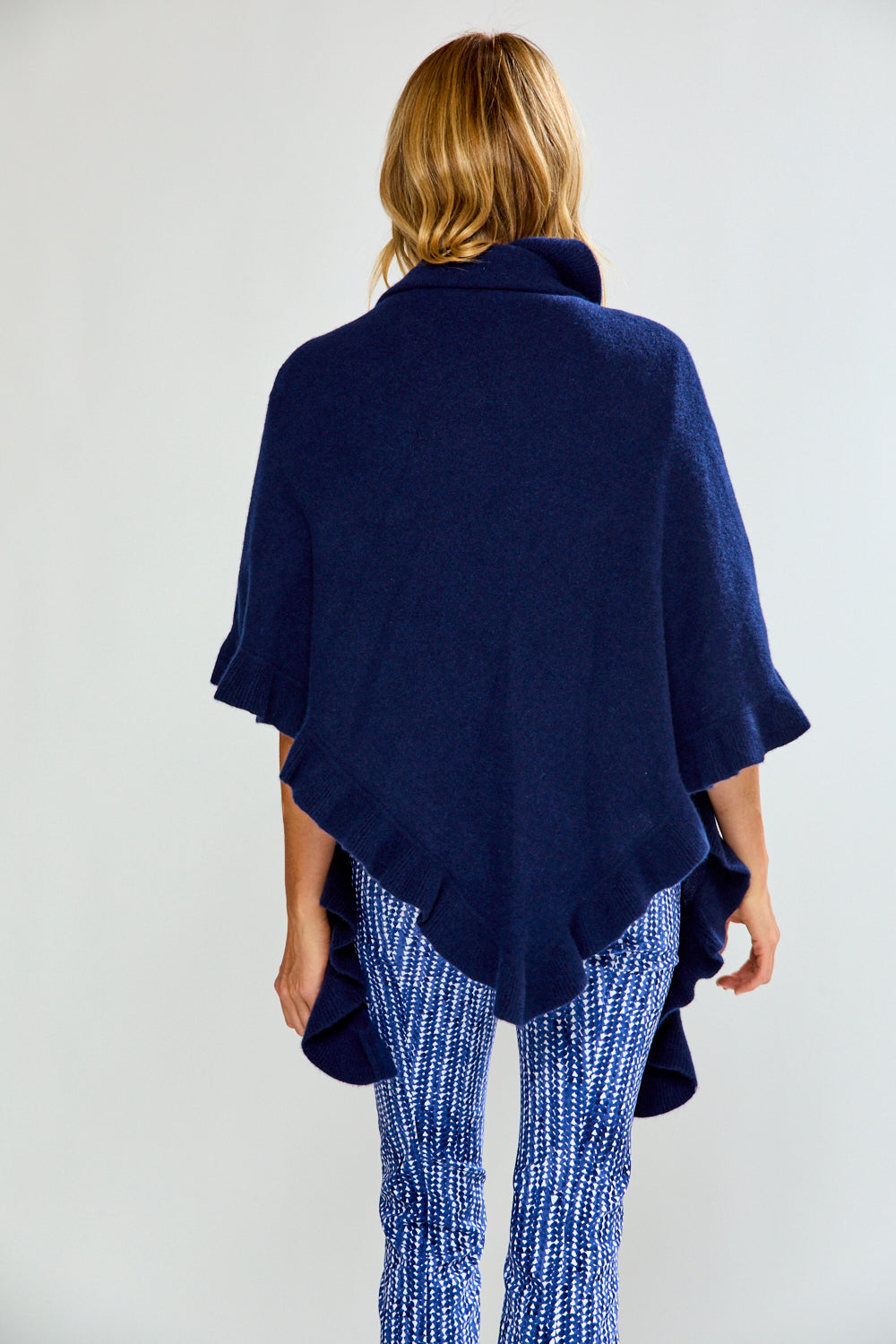 Woman wearing a navy blue ruffle triangle wrap over a white top and blue patterned pants on a white background