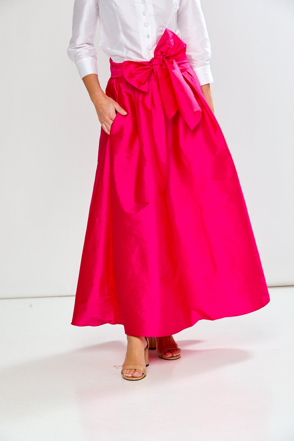 Person wearing a bright pink skirt with a white top on a white background
