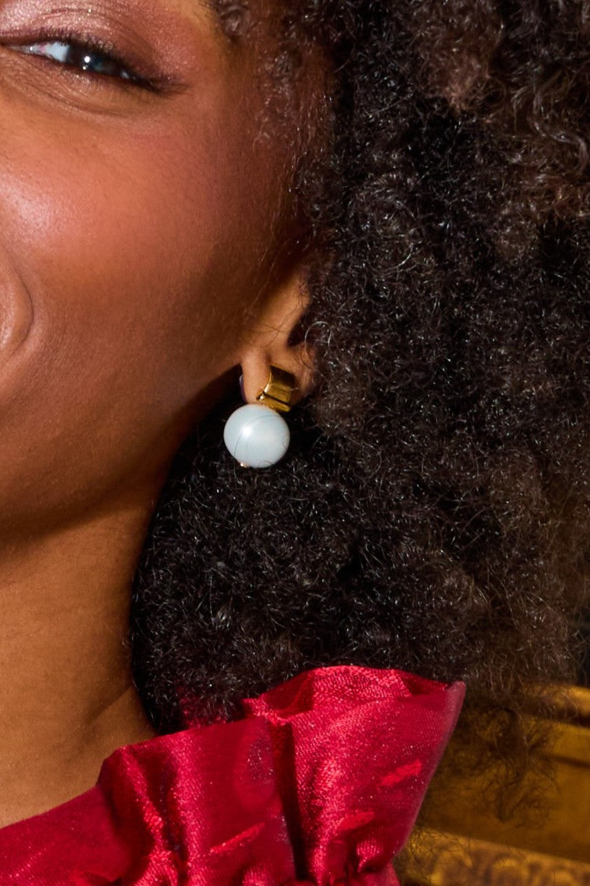 Close-up of a person wearing a pearl earring with a red garment and blurred background