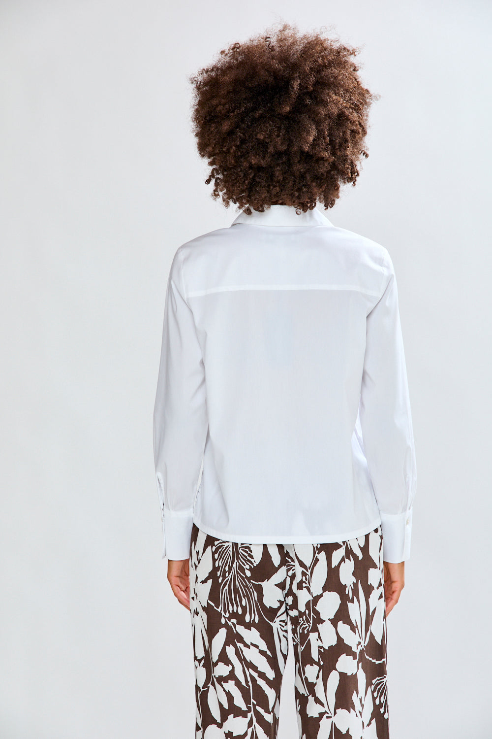 Woman wearing a white blouse and patterned pants against a plain background