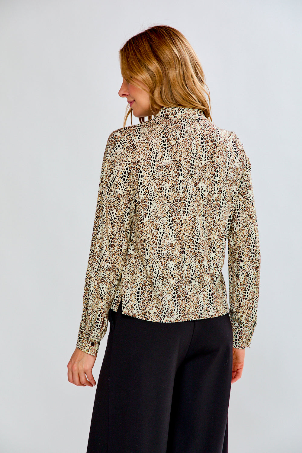 Woman wearing a patterned blouse and black pants against a plain background