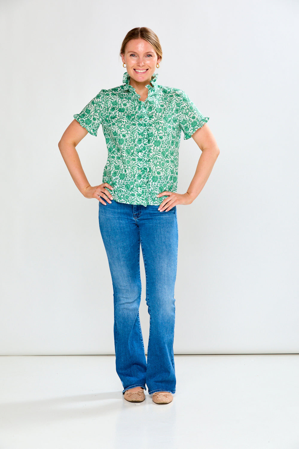 Woman wearing a green patterned shirt and blue jeans on a white background