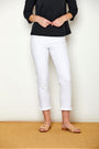 Person wearing a black top and white pants standing on a wooden floor with a white wall background