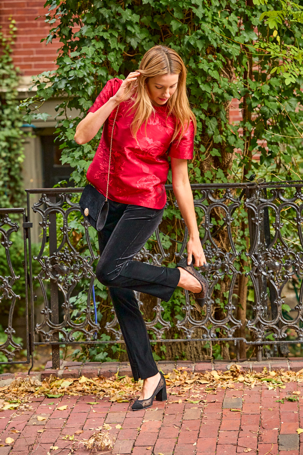 Woman wearing red blouse and black velvet pants while fixing her heel