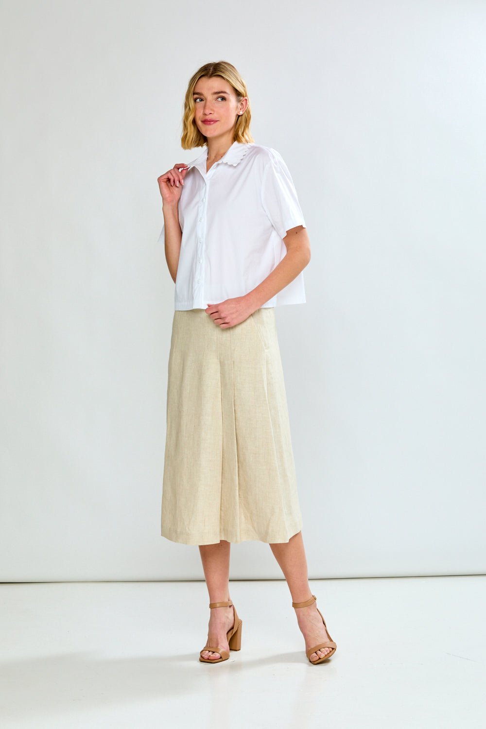 Woman wearing a white shirt and beige skirt against a white background