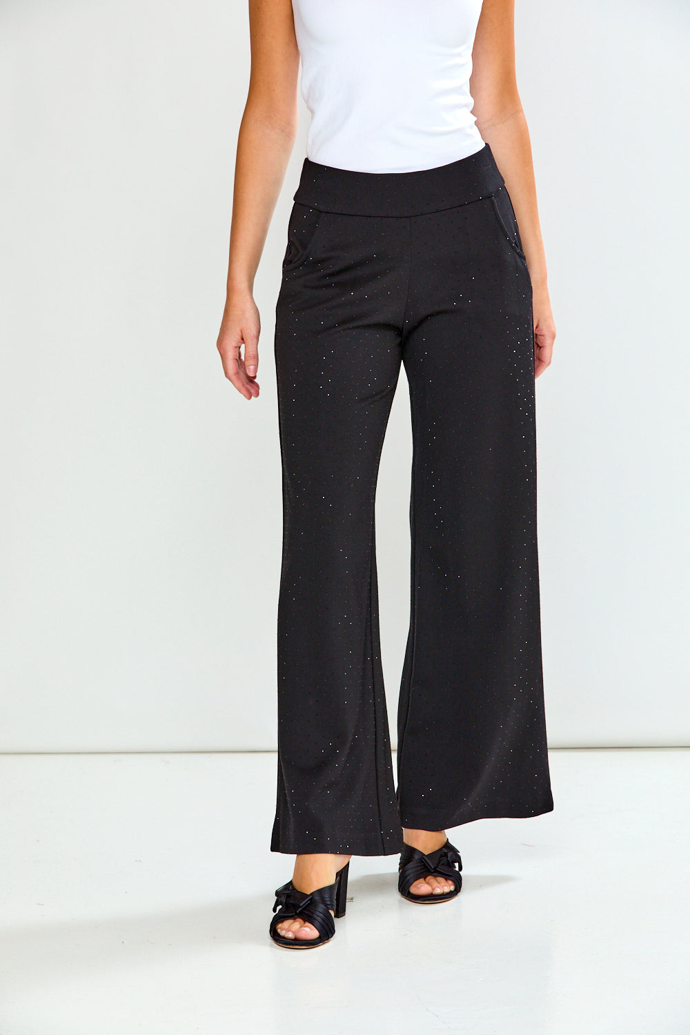 Person wearing black flared pants and a white top on a white background