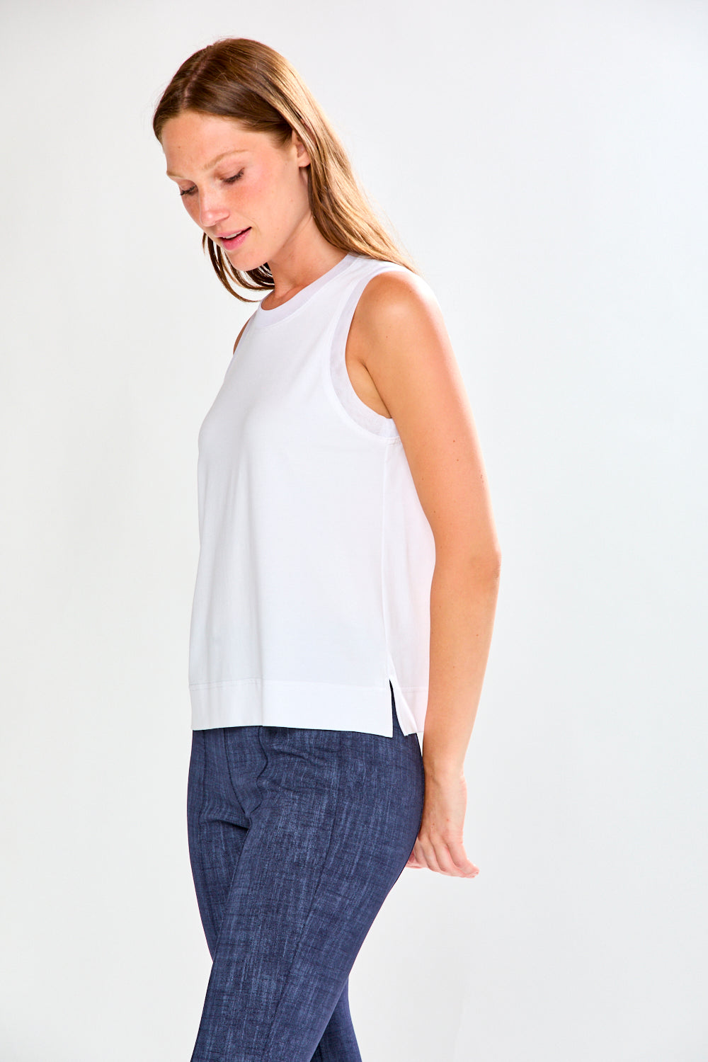 Woman wearing a white sleeveless top and blue pants on a white background