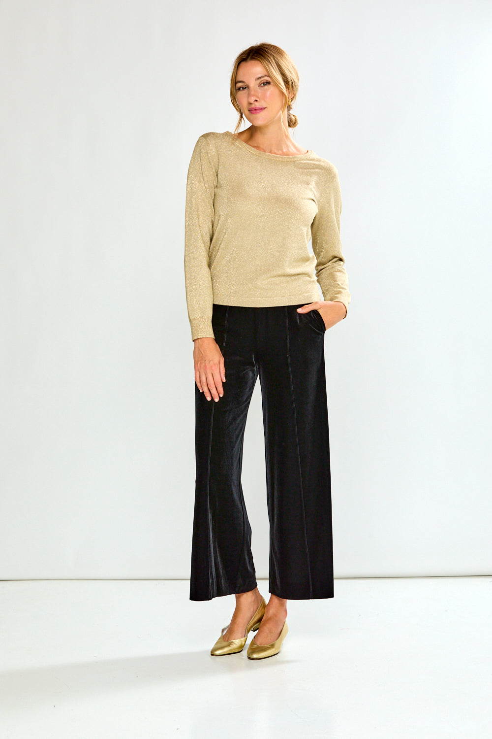 Woman wearing a gold sweater and black pants on a white background