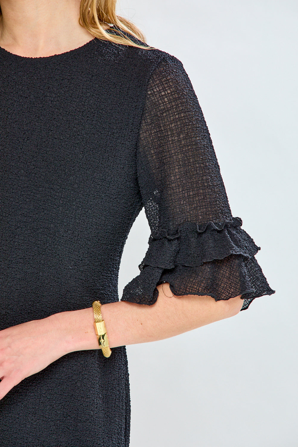 Black dress with sheer sleeves featuring ruffled cuffs on a white background
