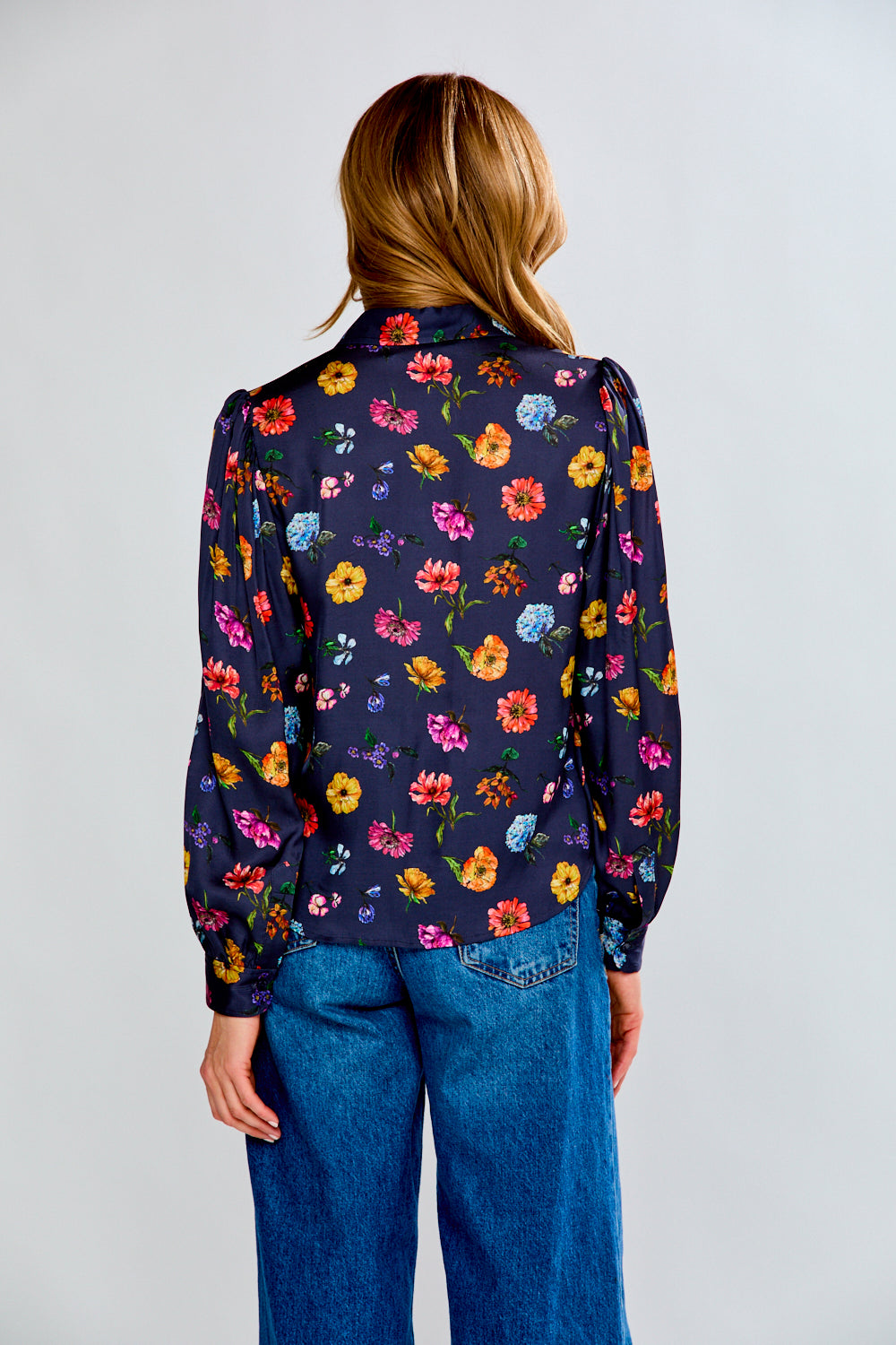 Person wearing a dark floral patterned shirt and blue jeans on a white background