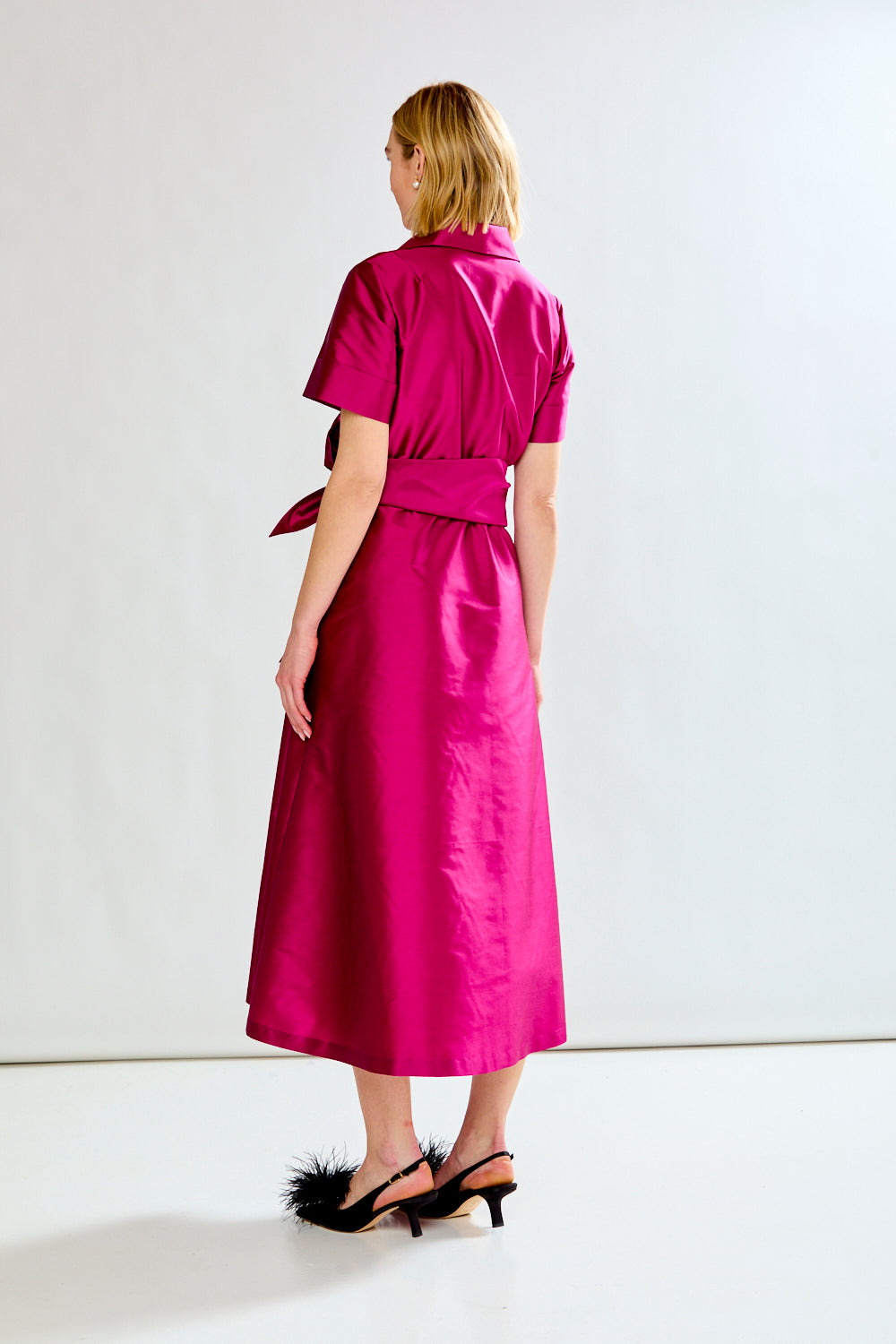 Woman wearing a bright pink dress with a belt on a white background