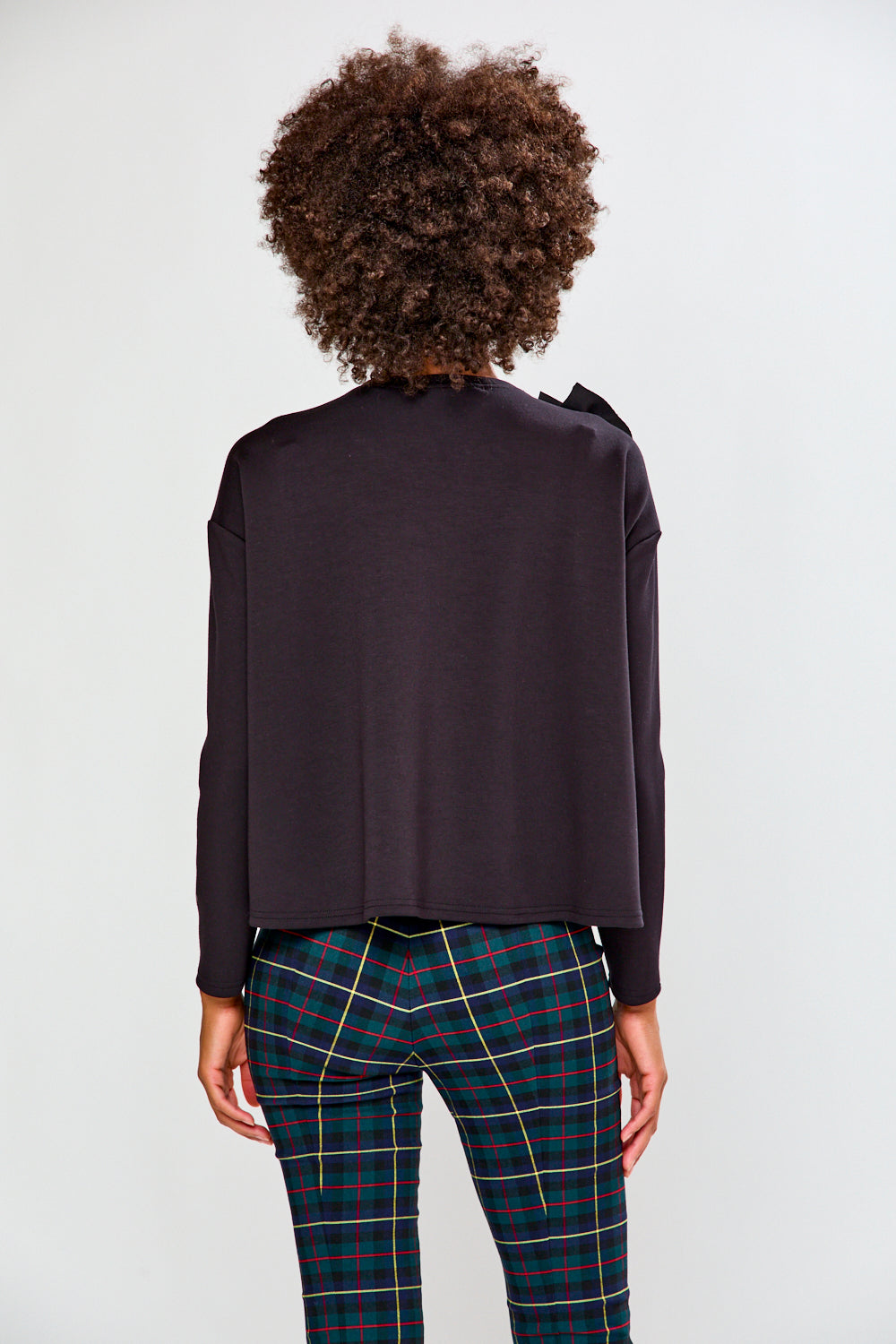 Woman wearing a black ruffled top and plaid pants against a white background