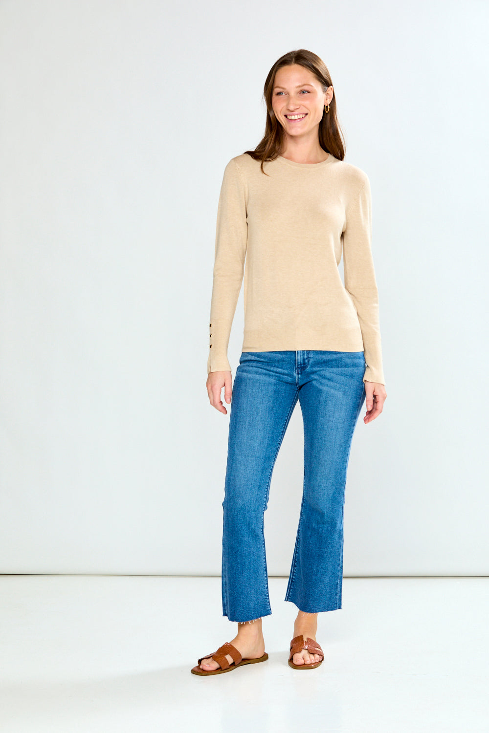 Woman wearing a sand sweater and blue jeans against a white background