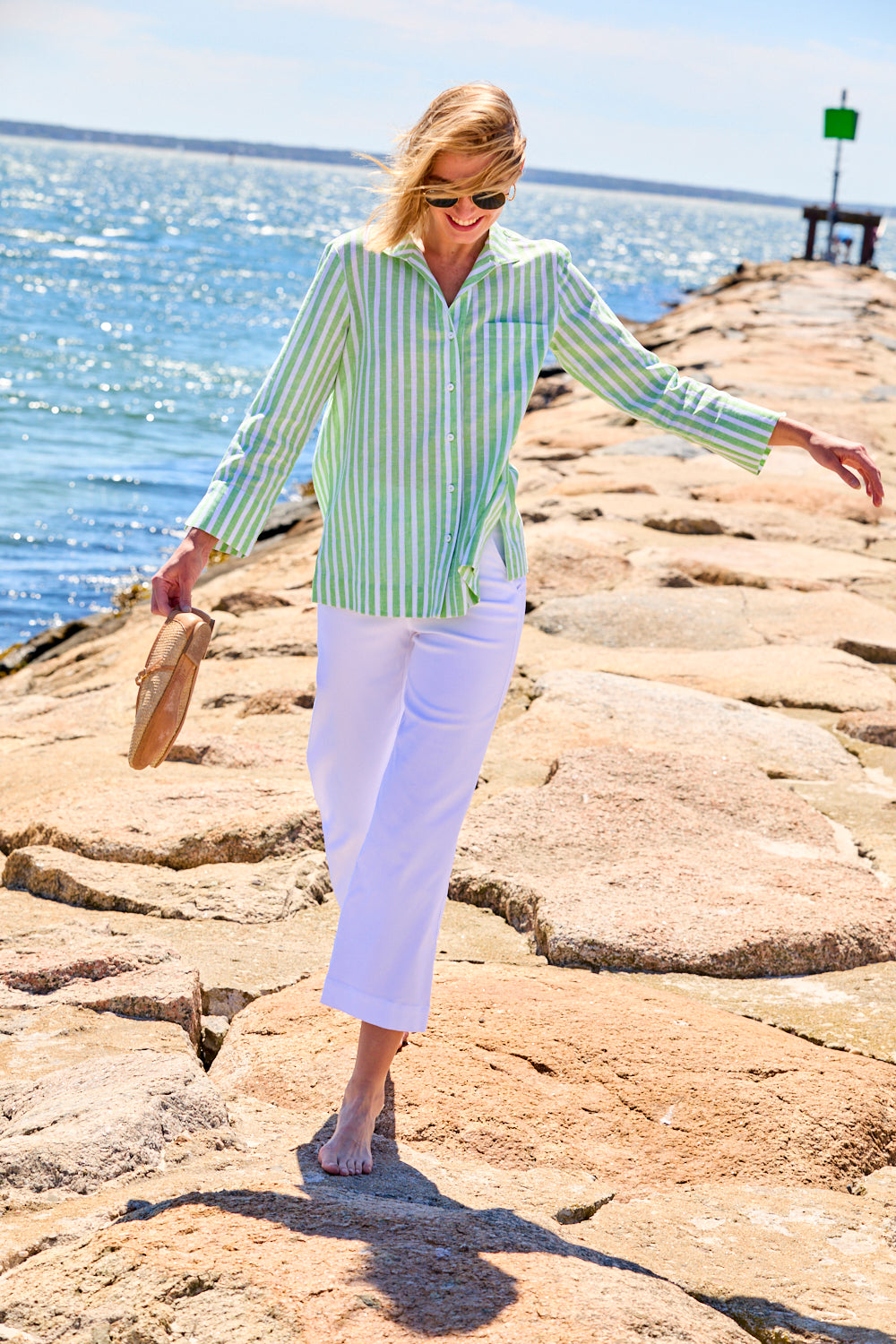 Woman in a striped shirt and white pants standing on rocks by the water
