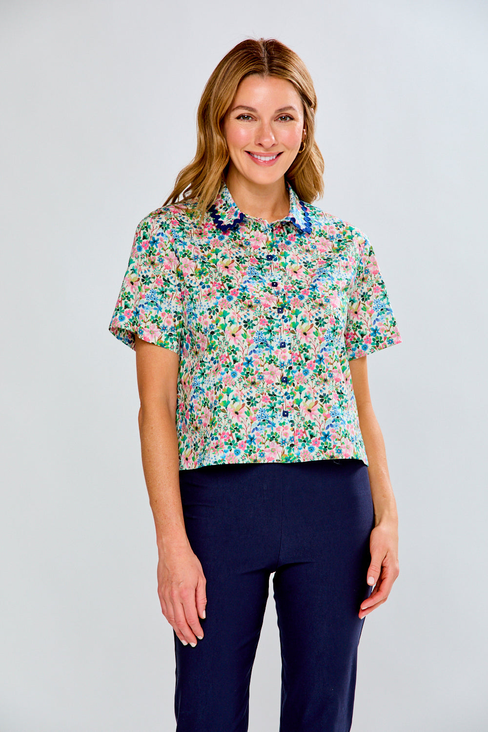 Woman wearing a floral blouse and navy pants on a light gray background