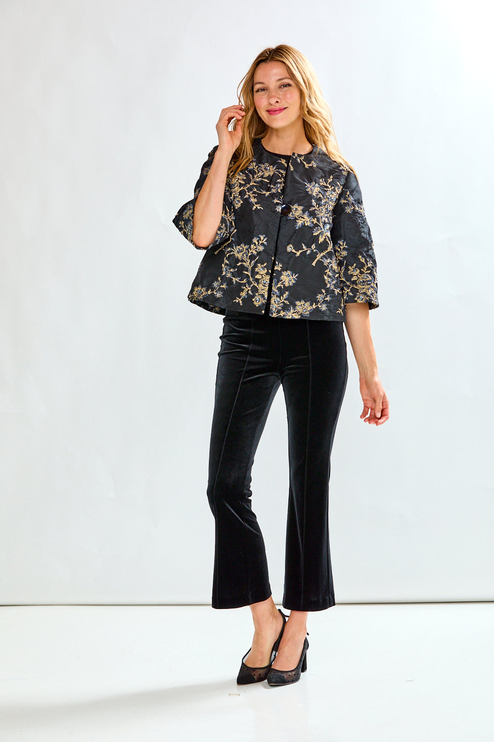 Woman wearing a black floral blouse and black pants on a white background