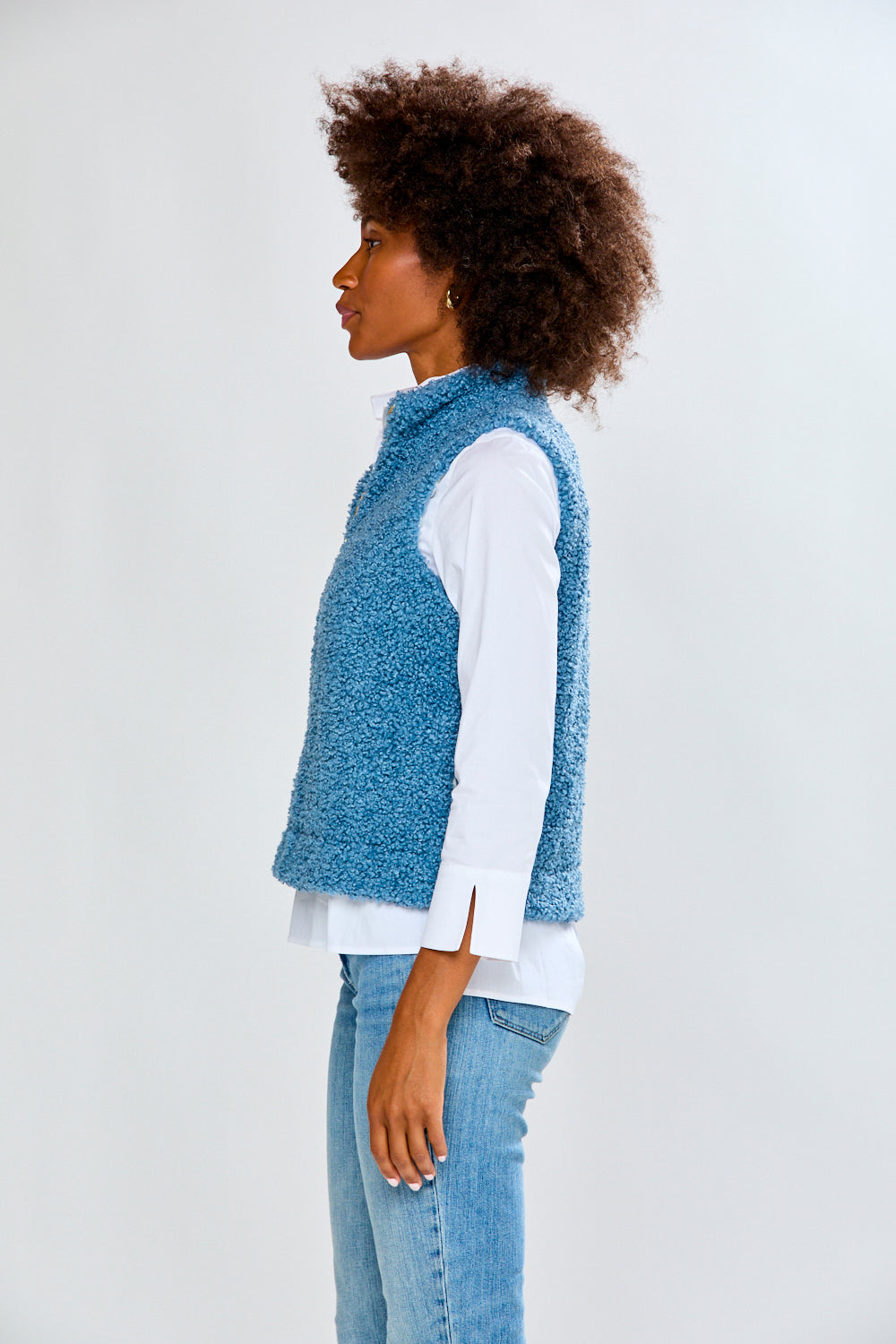 Woman wearing a blue textured vest over a white shirt and jeans on a white background