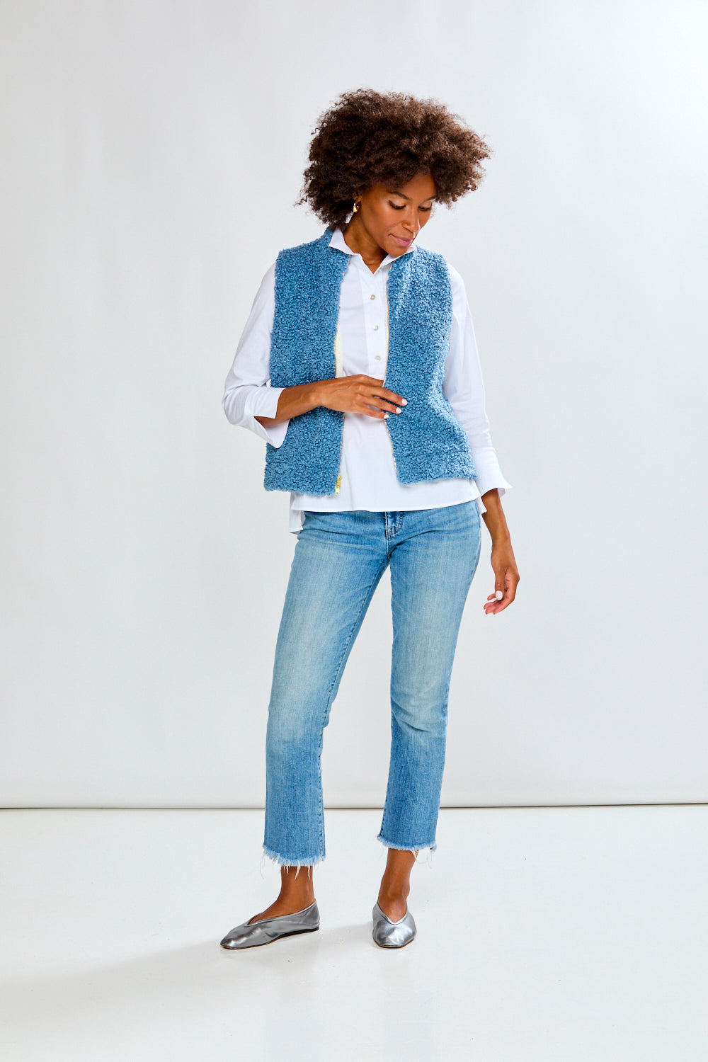 Woman wearing a blue textured vest over a white shirt and jeans on a white background