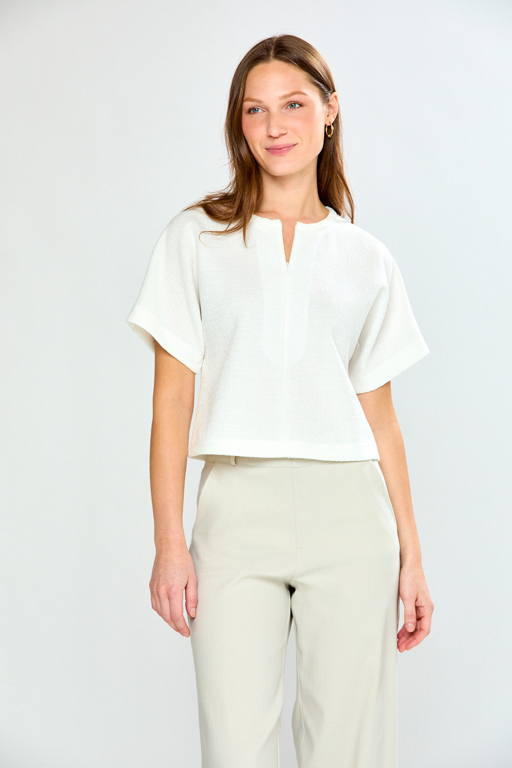 Woman wearing a white blouse and beige pants against a plain background