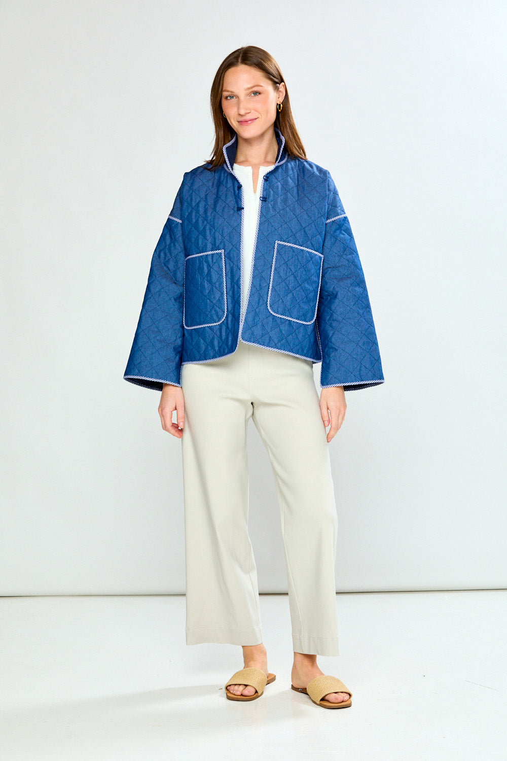 Woman wearing a blue jacket and white pants on a plain background