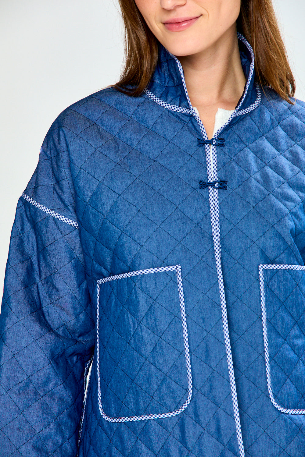 Person wearing a blue quilted jacket with white stitching on a plain background