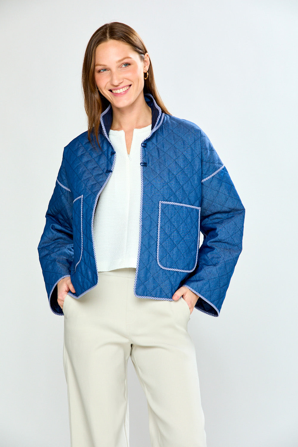 Woman wearing a blue quilted jacket with white pants on a light gray background