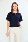 Woman wearing a navy blue top and white pants on a white background