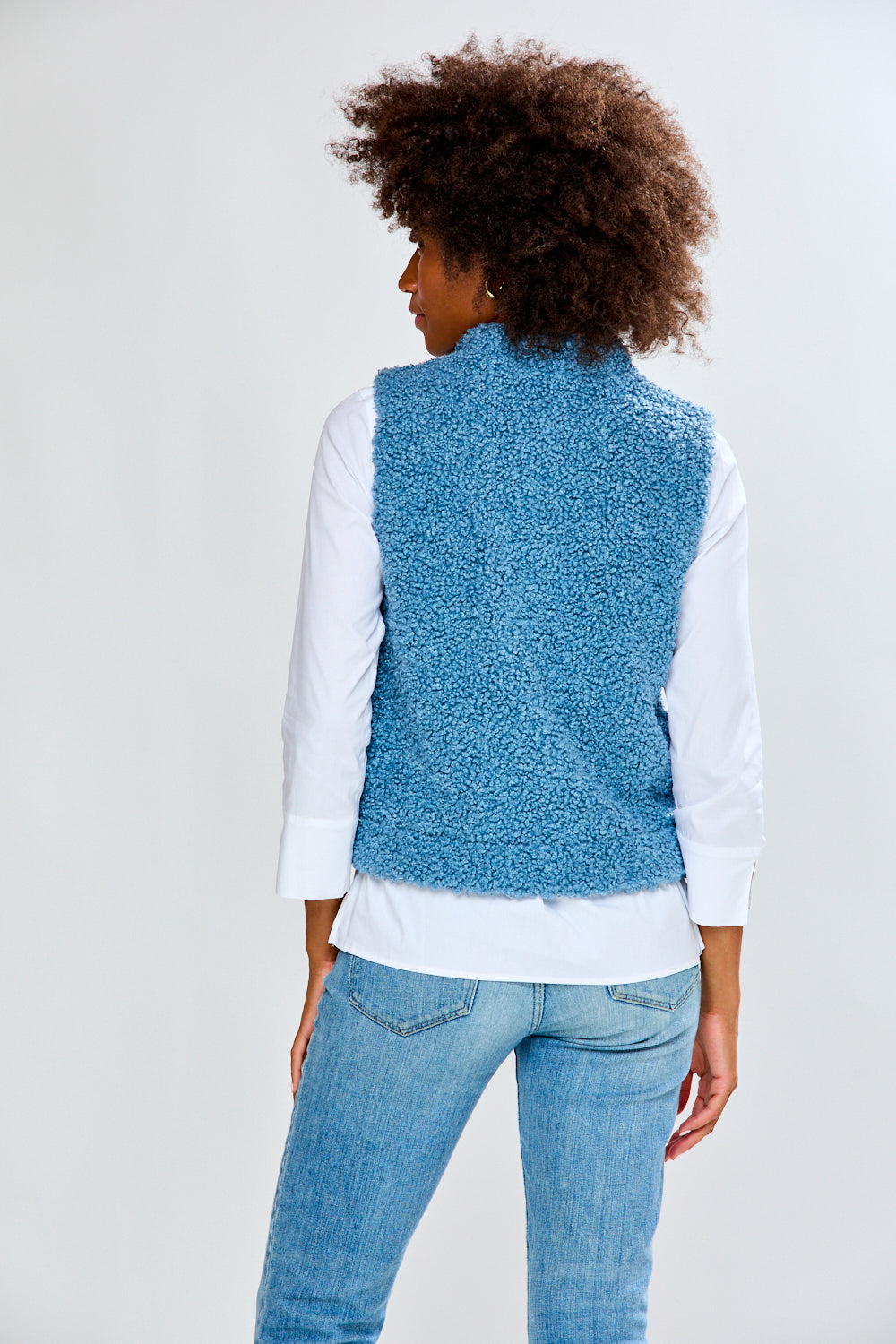 Woman wearing a blue textured vest over a white shirt and jeans on a white background