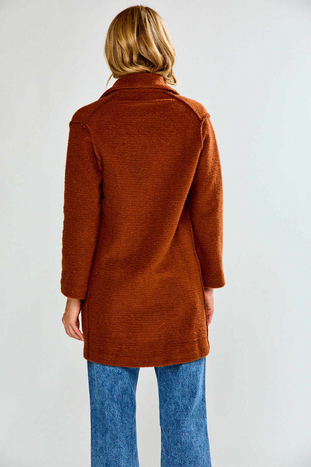 Woman wearing a brown coat over a white turtleneck on a white background