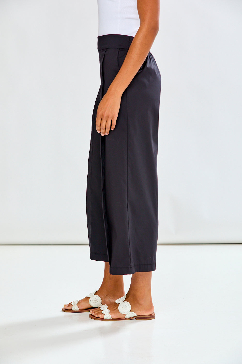 Woman wearing black wide-leg pants and white sandals on a white background