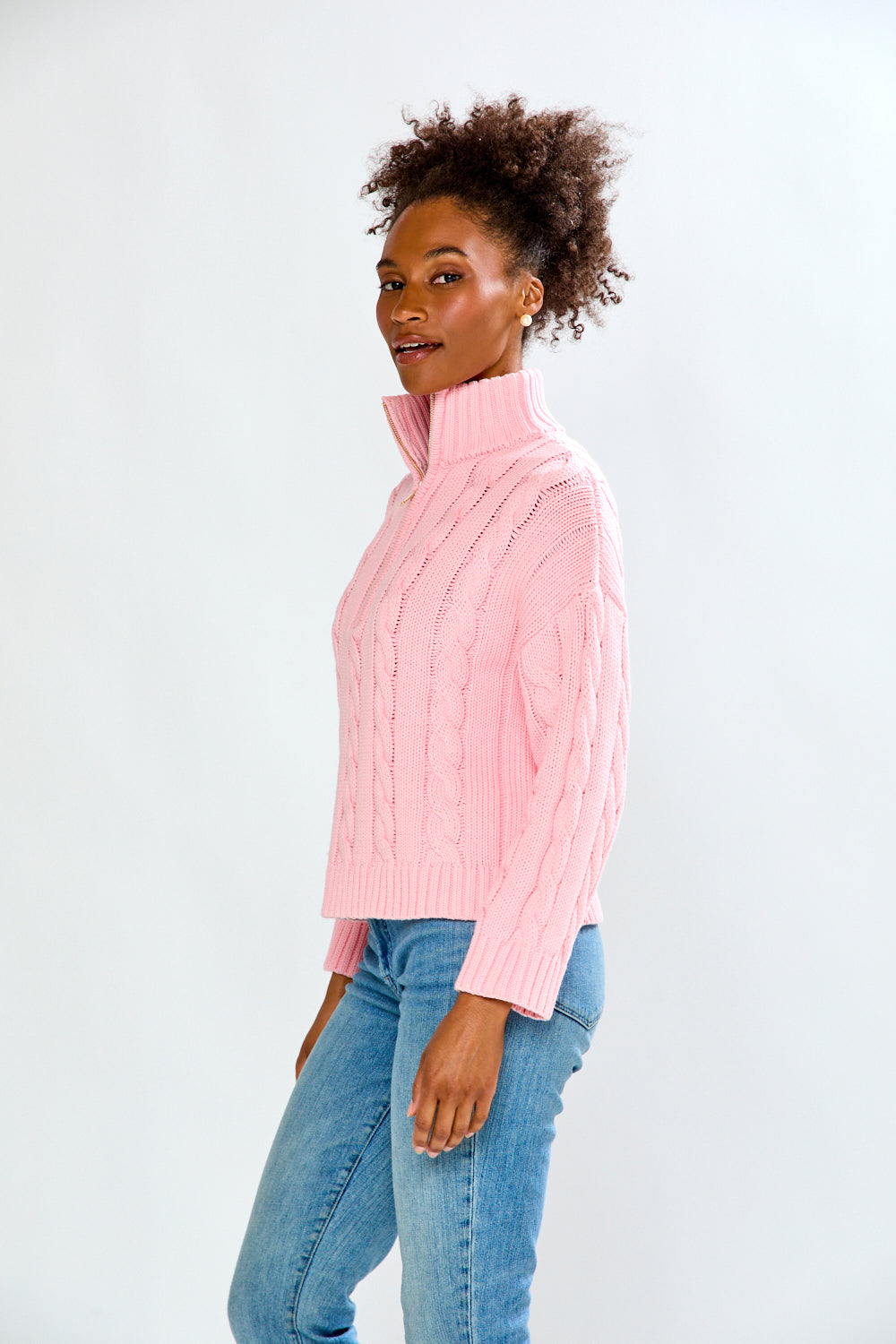 Woman wearing a pink cable knit sweater and blue jeans on a white background