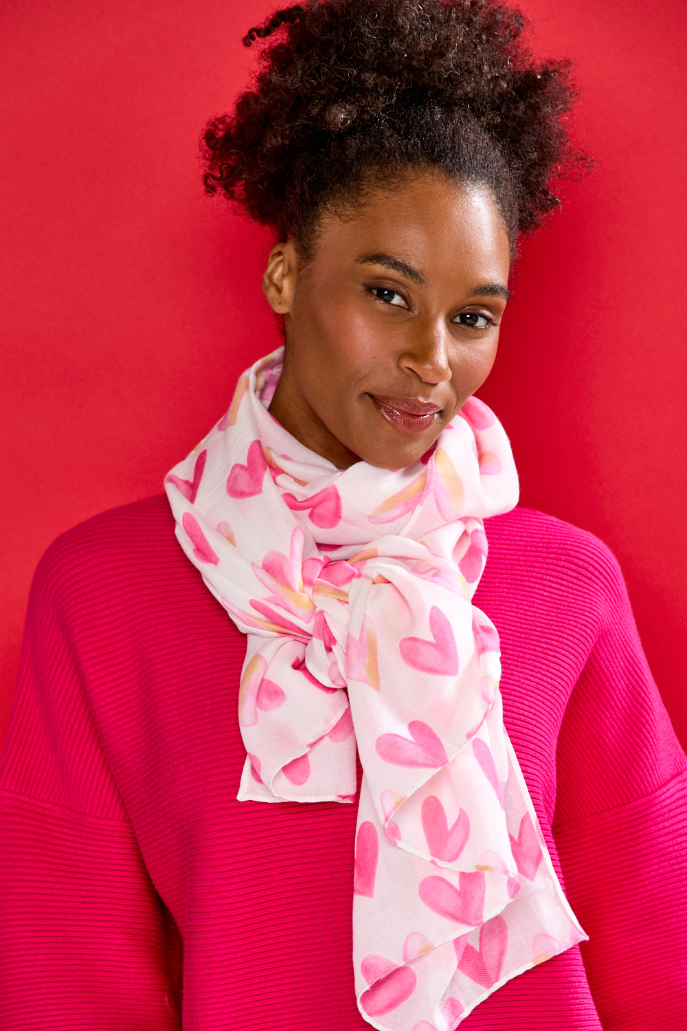 Woman wearing a pink sweater and heart-patterned scarf against a red background