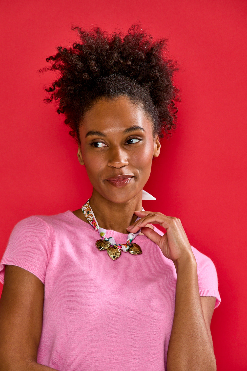 Woman wearing a pink shirt and colorful necklace against a red background