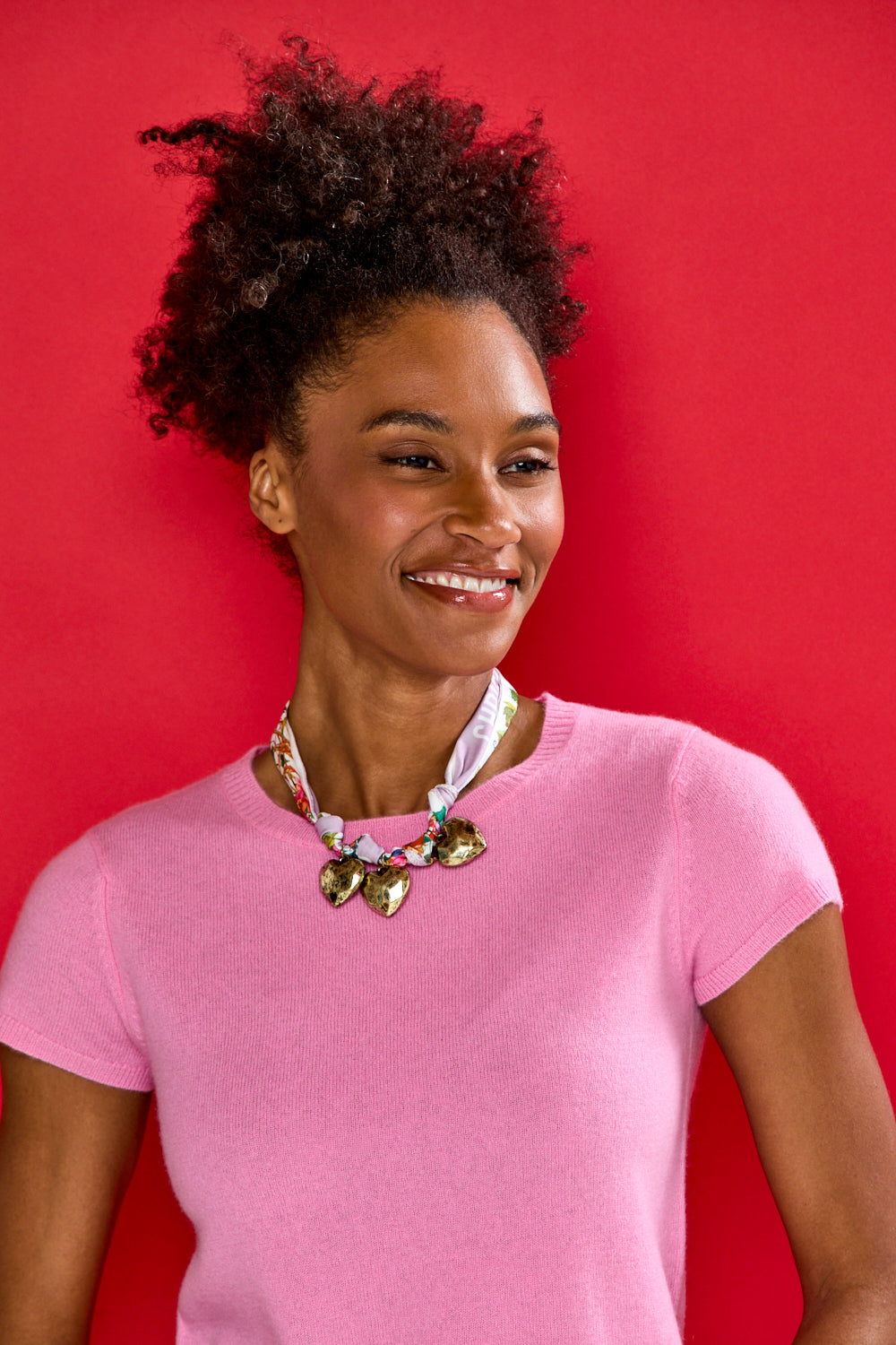 Woman wearing a pink shirt with a colorful necklace against a red background