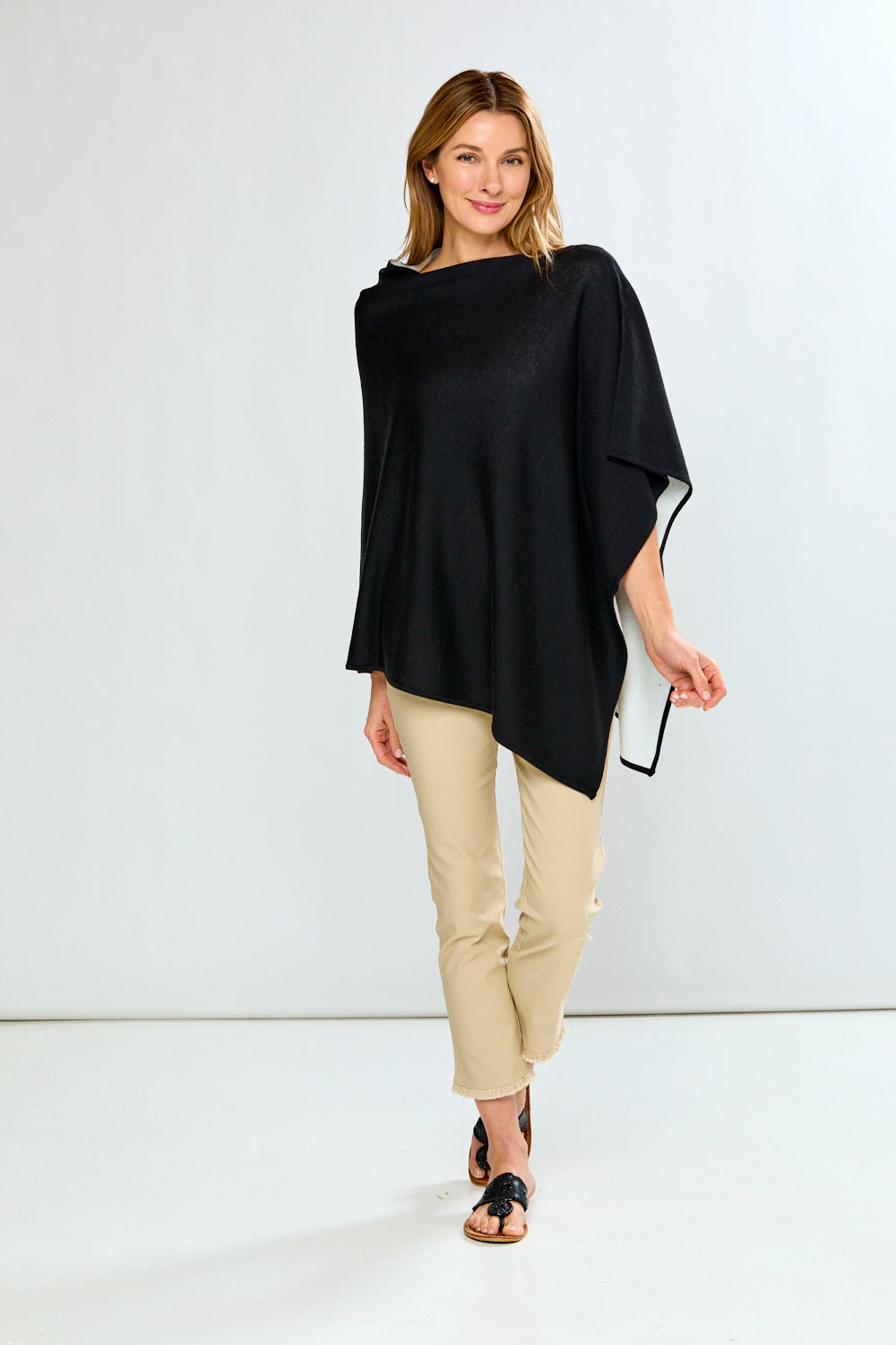 Woman wearing a black poncho and beige pants against a white background