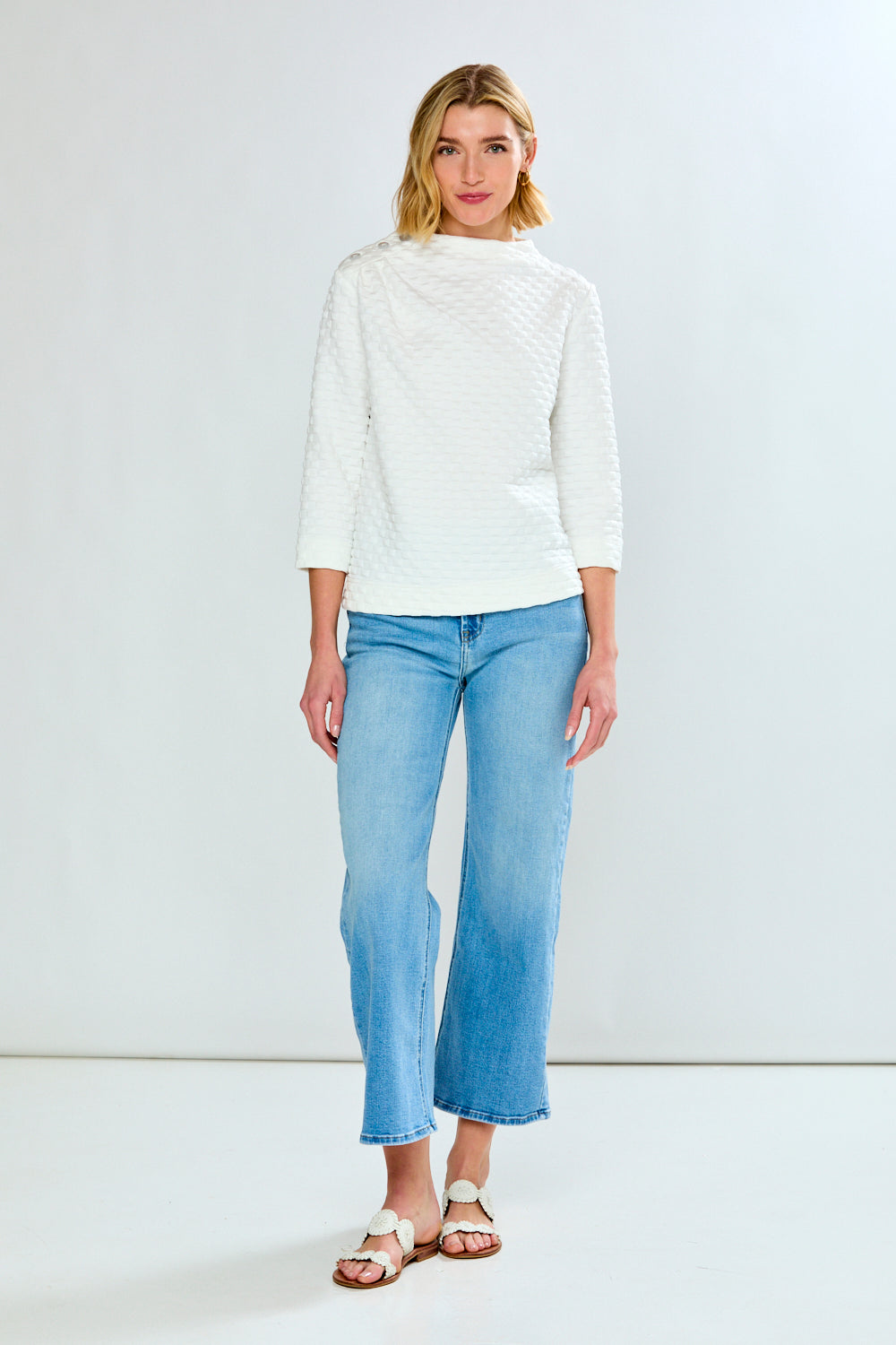 Woman wearing a white sweater and light blue jeans against a white background