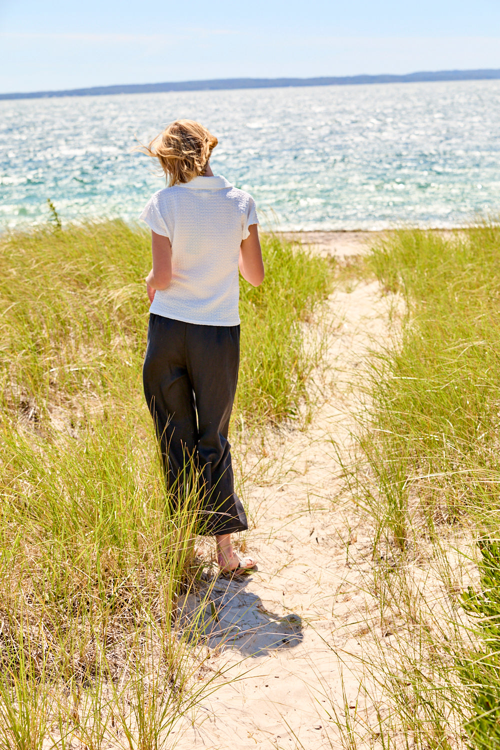 Woman walking along a sandy path towards the ocean