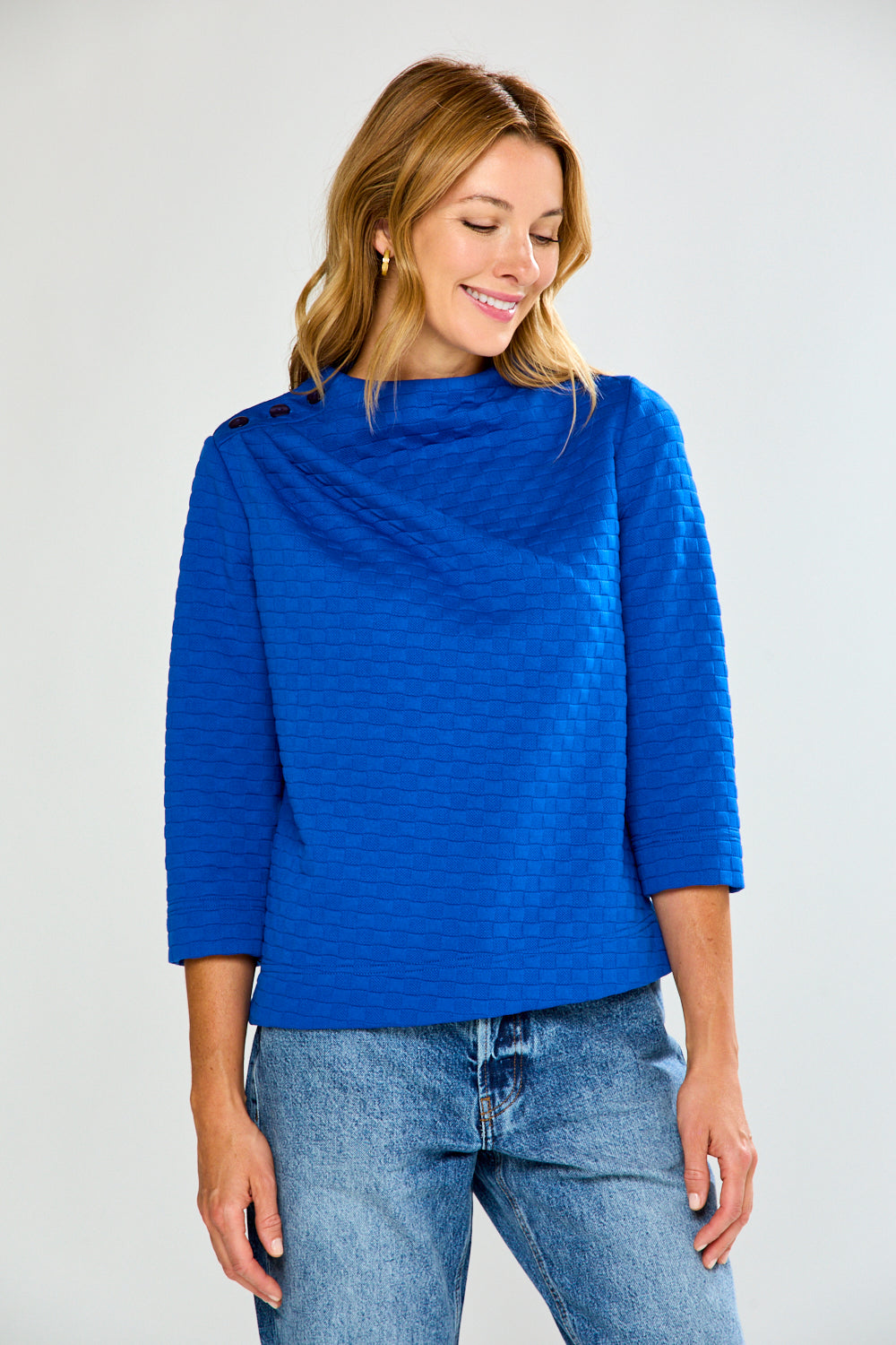 Woman wearing a blue textured top and jeans on a white background