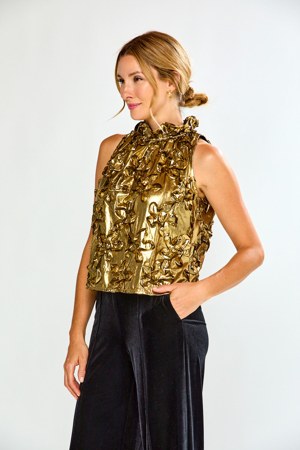 Woman wearing a gold metallic top and black pants on a white background