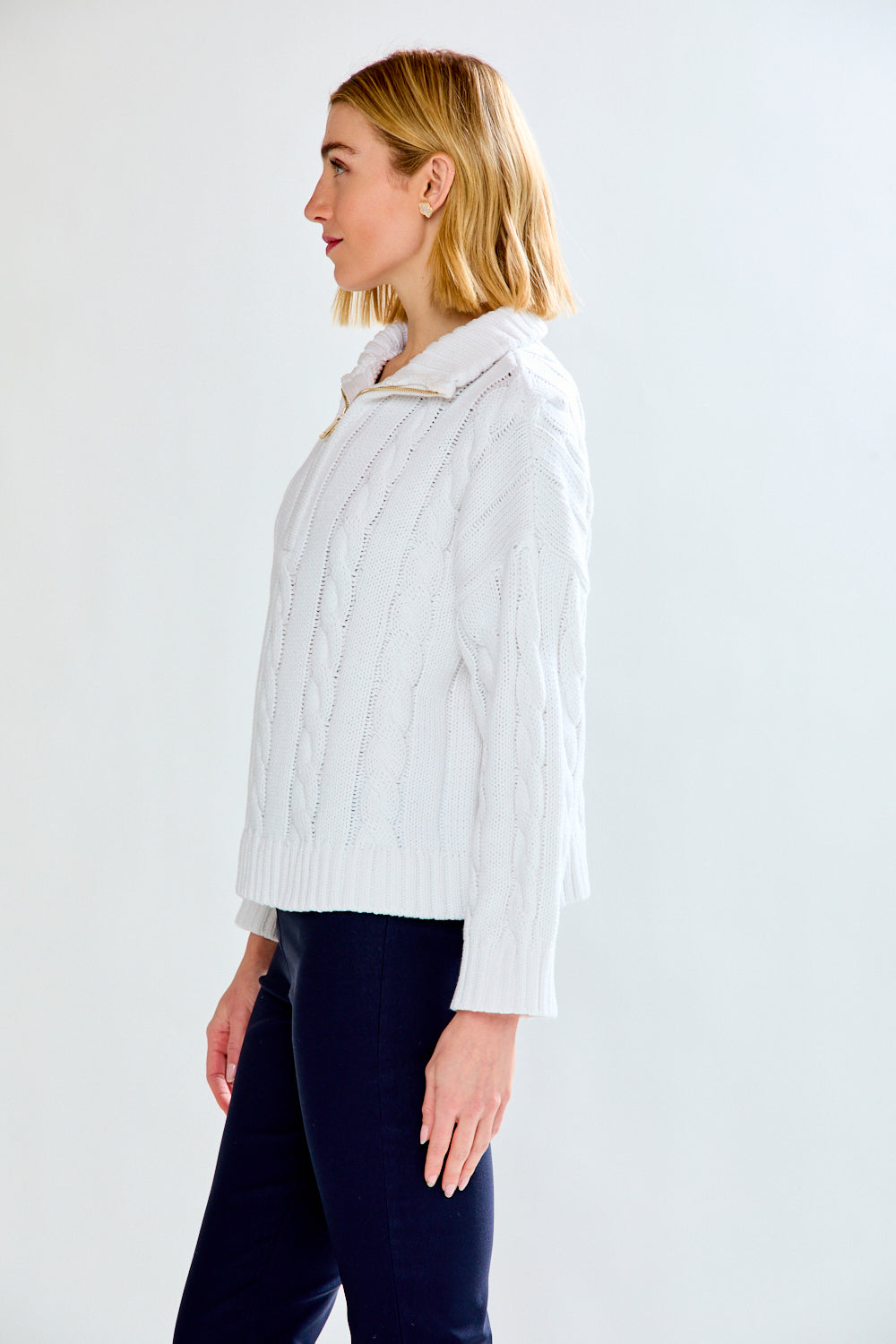Woman wearing a white cable knit sweater against a plain background