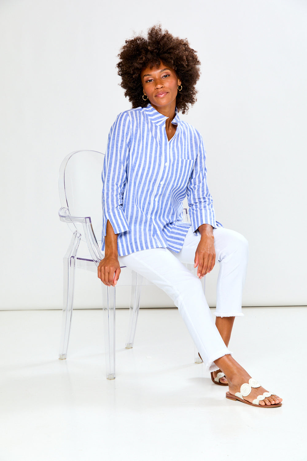 Woman sitting on a chair wearing a blue and white striped shirt and white pants.