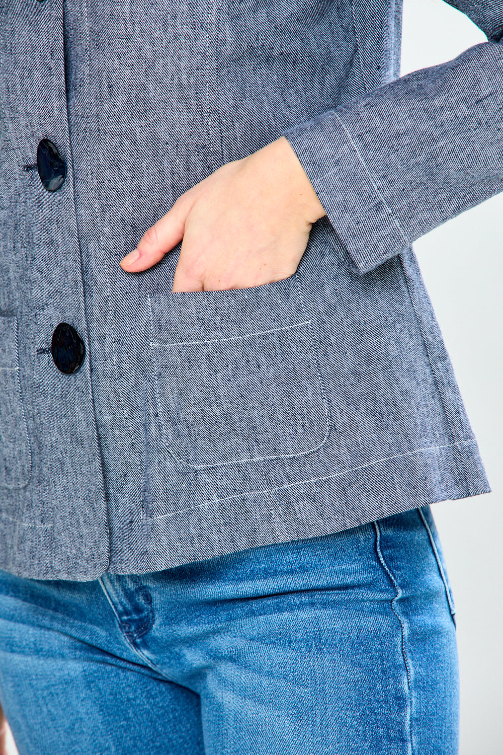 Gray blazer with black buttons worn by a person, on a white background