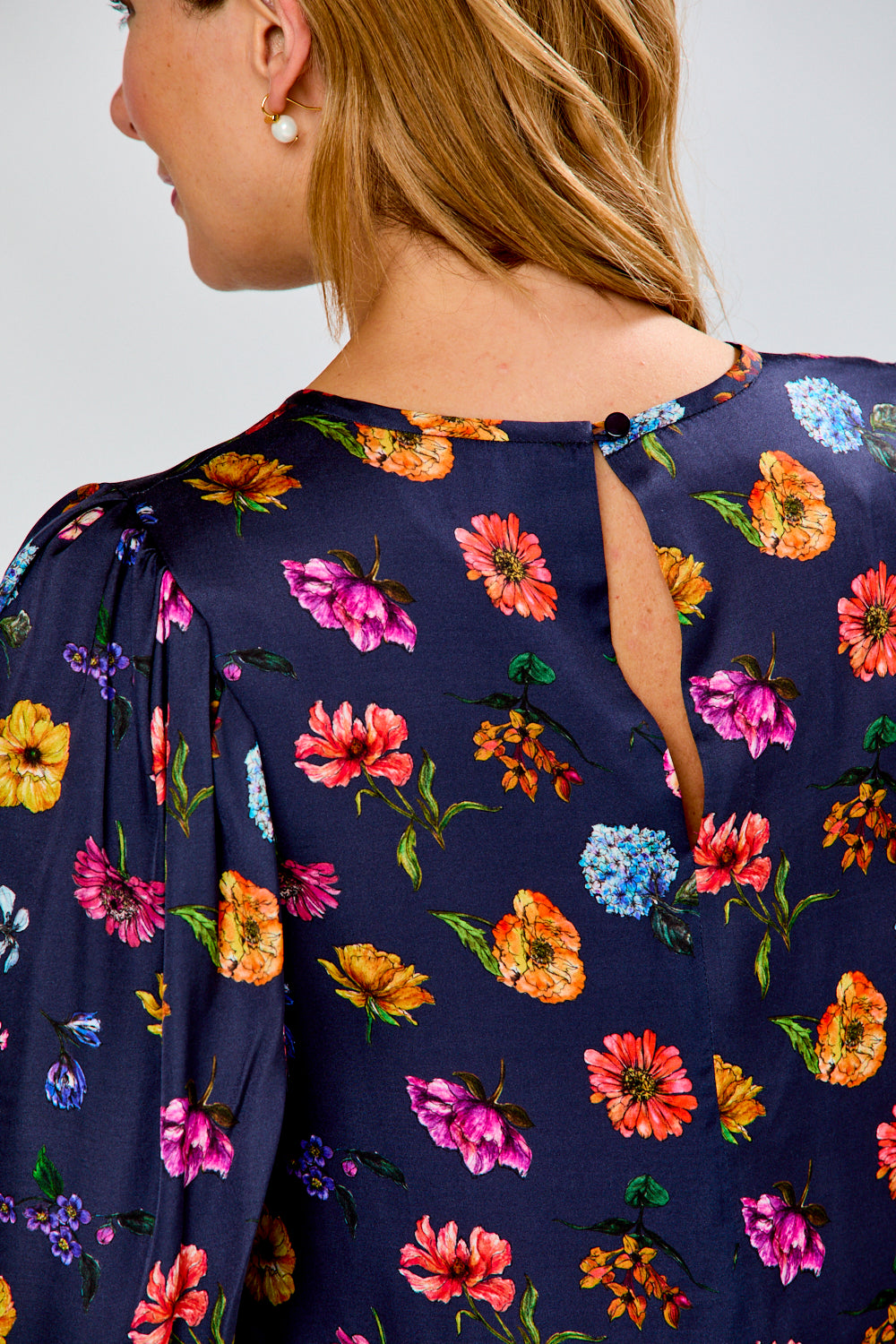 A woman modeling a navy blue short-sleeve shift dress with a colorful floral print, paired with tan slide sandals, against a plain white studio background.