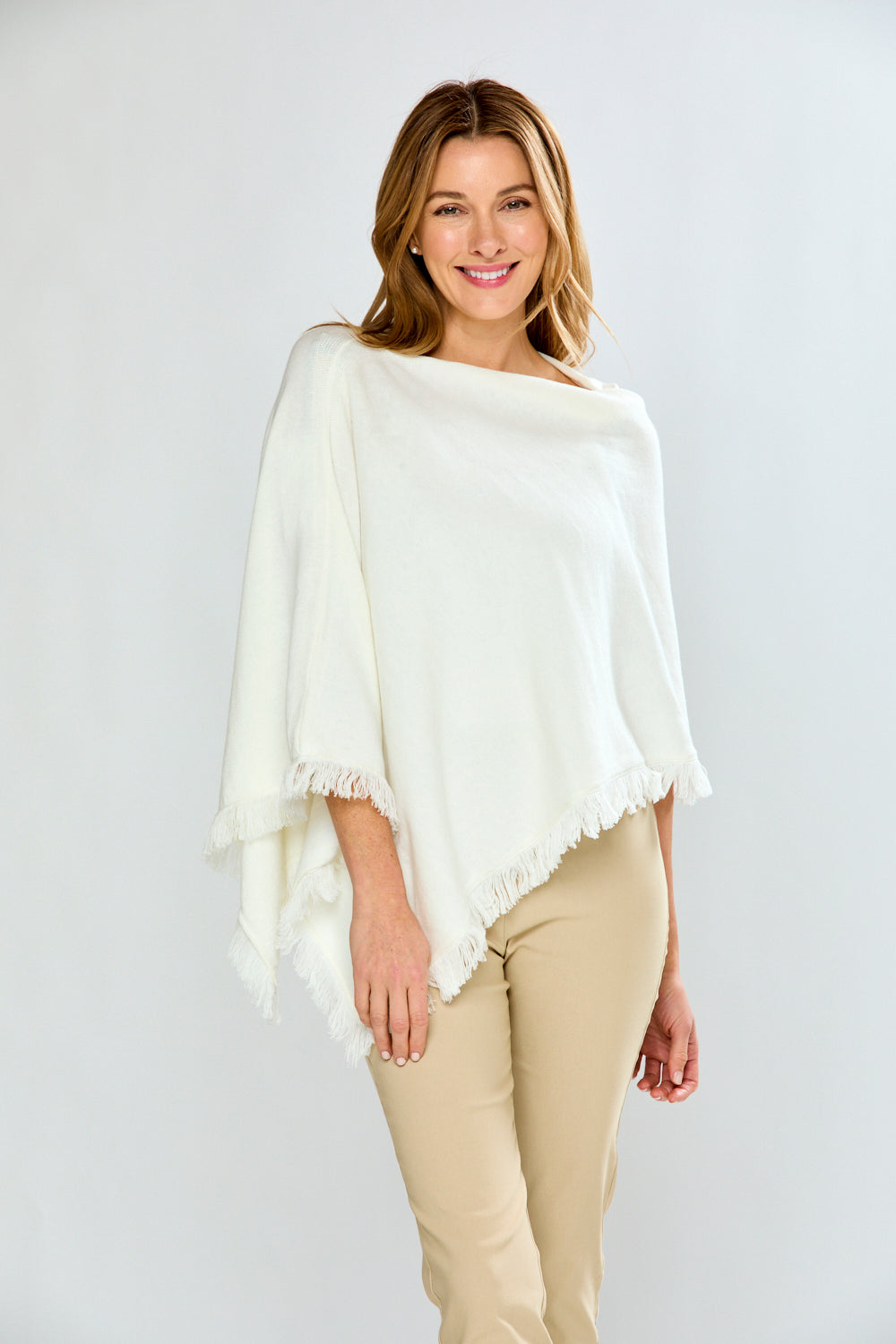 Woman wearing a white poncho with beige pants on a plain background