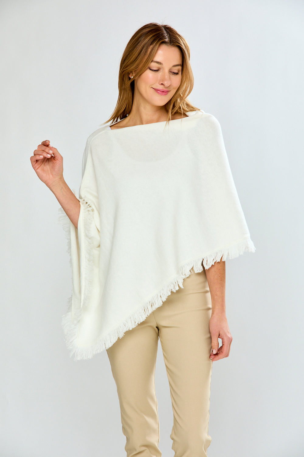 Woman wearing a white poncho with beige pants on a plain background