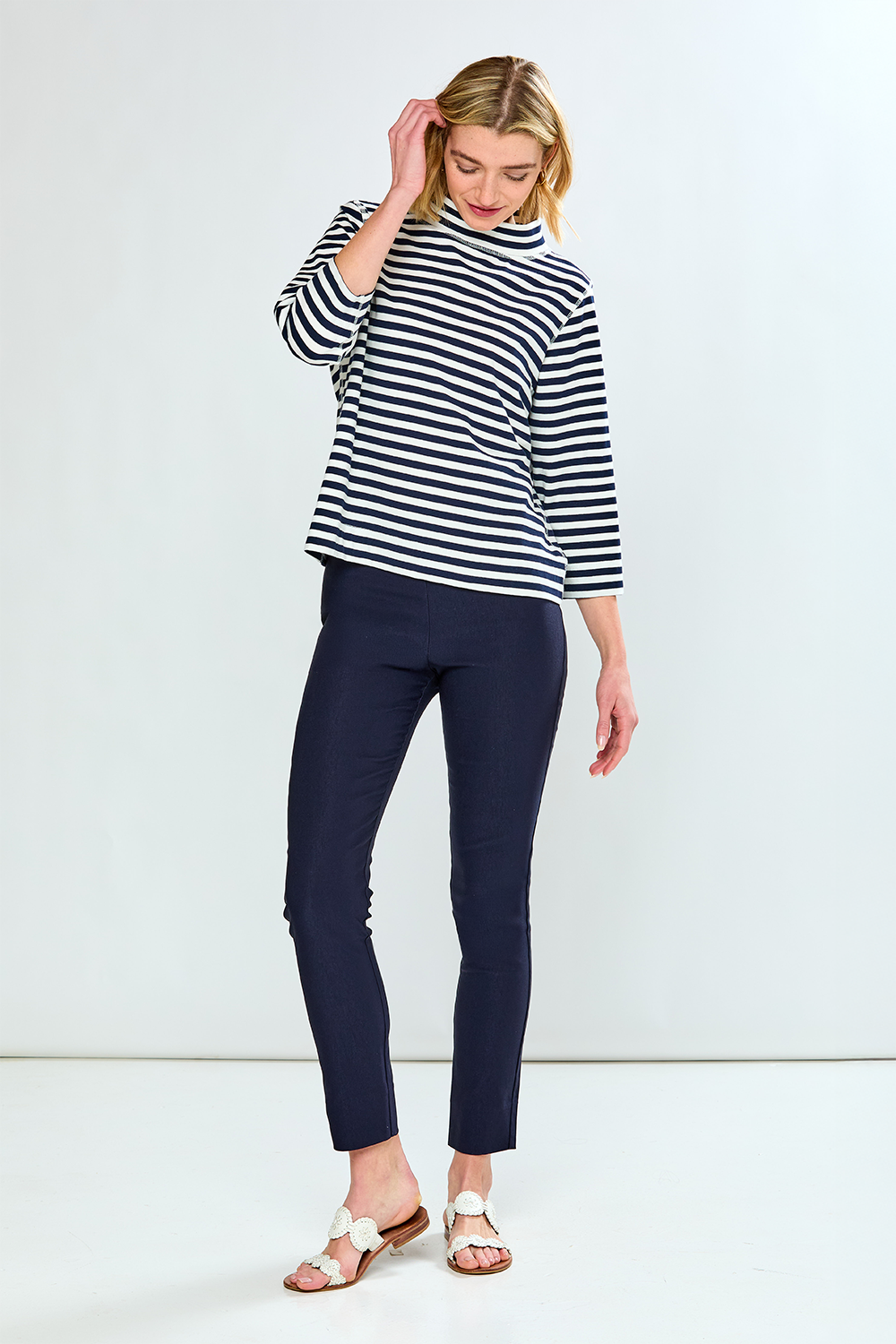 Woman wearing a black and white striped shirt and navy pants on a white background