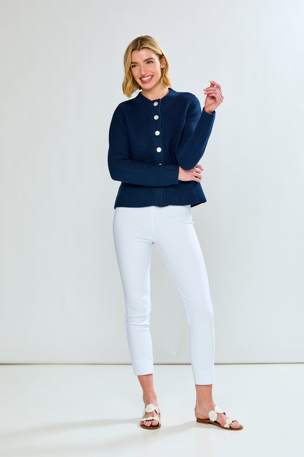 Woman wearing a navy blue cardigan and white pants on a white background